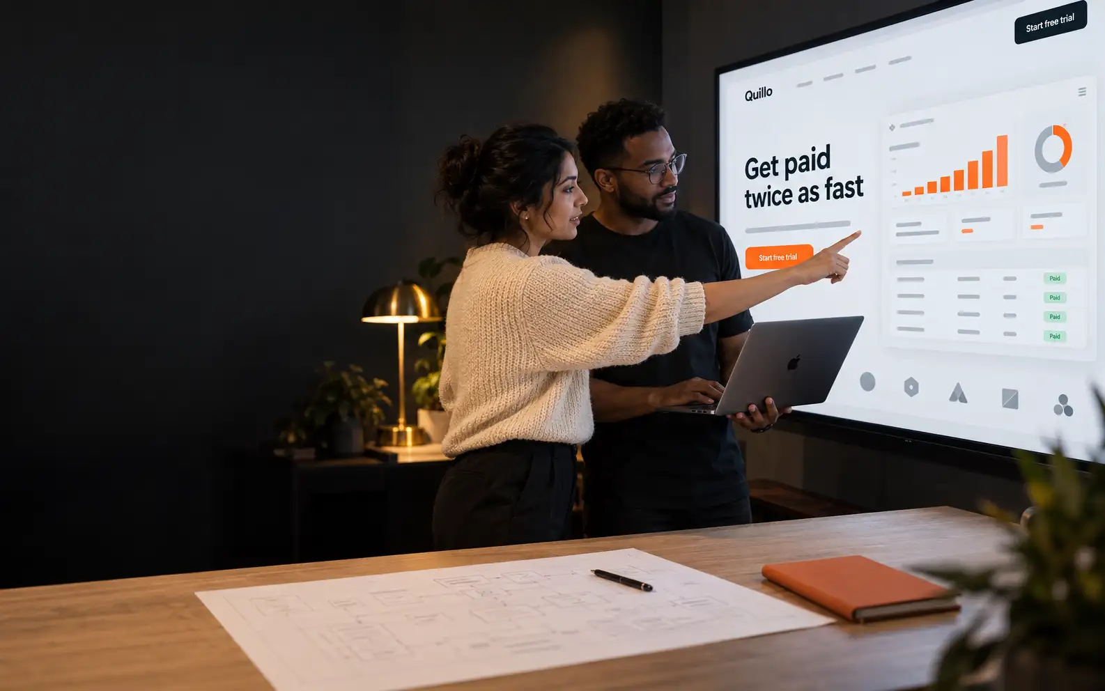 A designer and a developer reviewing a client homepage on a large wall display in a dim studio